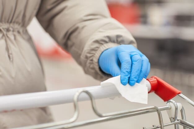 A close-up shot of a retail employee sanitizing a shopping cart handle with a disinfectant wipe. The focus is on the action of cleaning and the gloved hand of the employee.