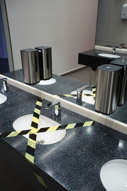 A well-stocked restroom sink area in a retail store. The scene includes a touchless soap dispenser, neatly arranged paper towels, and a small sign reminding users to wash their hands.