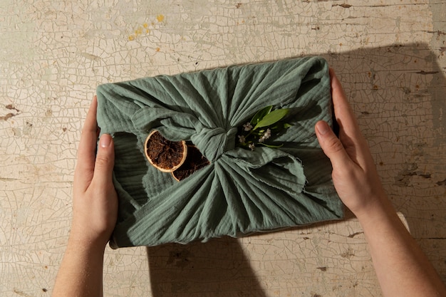 Close-up of a hand holding a package made from recycled cardboard with a clear label indicating its biodegradability. The background is blurred, highlighting the focus on sustainable materials.